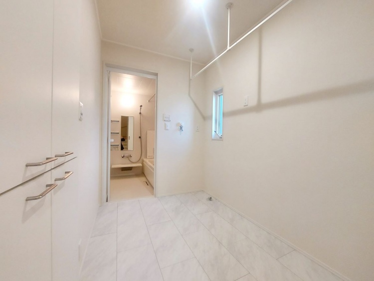 天井から物干し竿が吊るされた部屋で、小さな窓とすりガラスの引き戸からほのかな光が差し込んでいます。