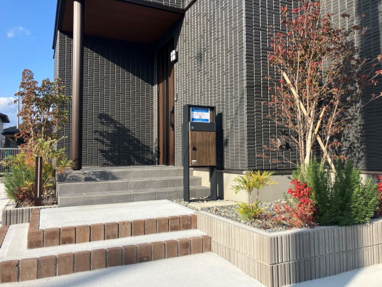 玄関まで続く段差のあるアプローチには、小さな植栽とポストが並び、家に入る前の穏やかな空間が広がっています。