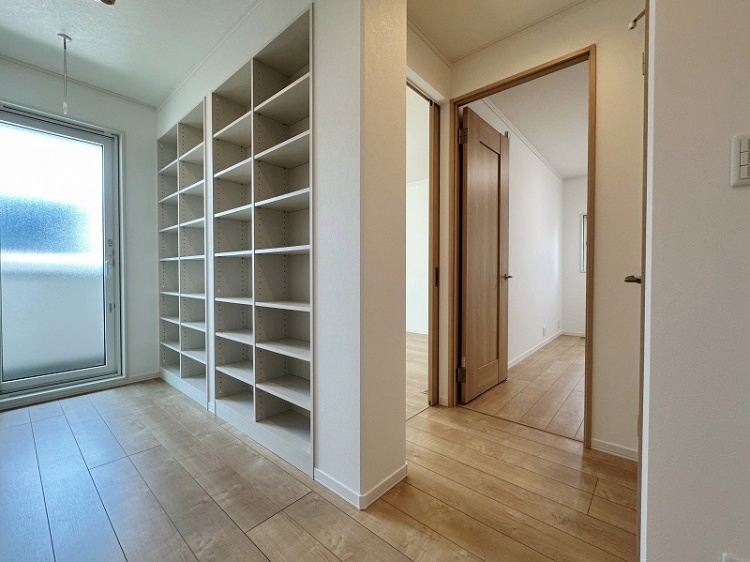 広々とした廊下に並ぶ収納棚。ガラス扉から光が差し込み、廊下の先には別の部屋に続く木製のドアが見える。