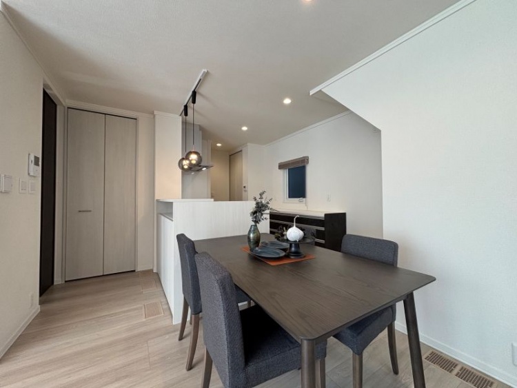 白を基調としたリビングダイニング。ダイニングテーブル、椅子、ペンダイトライトが設置されたカウンターキッチンが見えます。