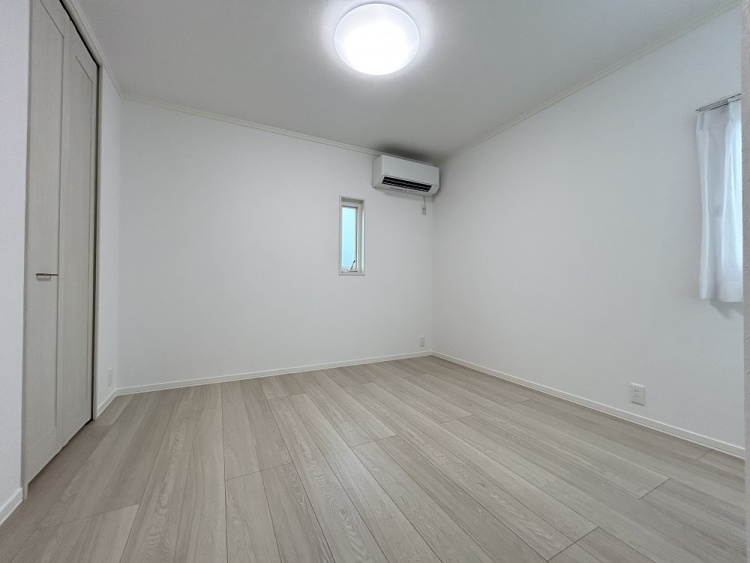 白い壁と明るい木目の床がやさしく調和した部屋で、小さな窓から自然光が入り、静けさと落ち着きが感じられます。