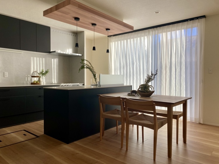 黒のアイランドキッチンと木製テーブルが調和するモダンなダイニングです。