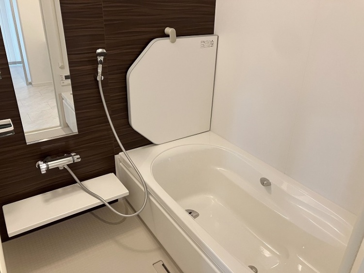 落ち着いた木目調の壁が印象的なバスルーム。広々とした白い浴槽があり、ゆったりとくつろげる空間です。シャワー横には鏡と収納棚が備え付けられ、使い勝手の良いデザイン。温かみと清潔感が共存する心地よい浴室です。