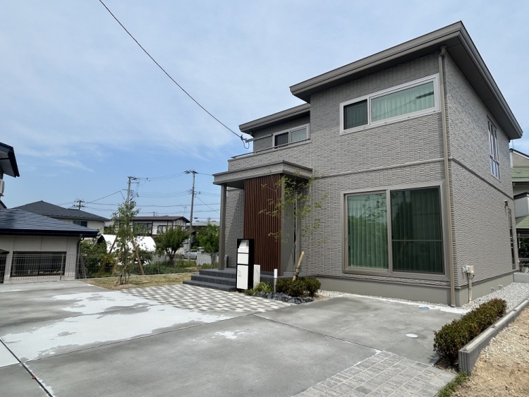 グレーの外壁の二階建て住宅の外観。玄関横に宅配ボックスが設置されています。前には駐車場が見えます。