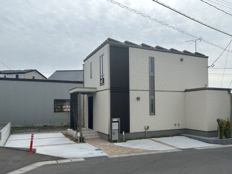 白い外壁とブラウンの縦格子を基調とした２階建て住宅の外観。駐車場も見えます。