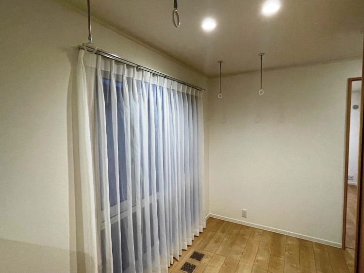 階段を上がった先の2階ホールで、白いカーテンから柔らかな光が差し込んでいます。天井には洗濯物を干すためのフックがあり、シンプルで明るい空間です。