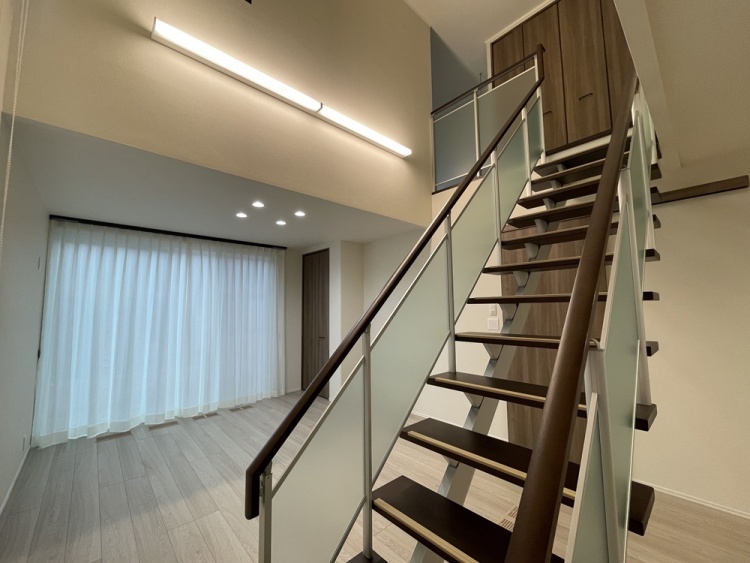 吹き抜けのあるリビングと、ガラス手すりを採用したオープン階段です。大きな窓と照明により、明るく開放感のある空間になっています。