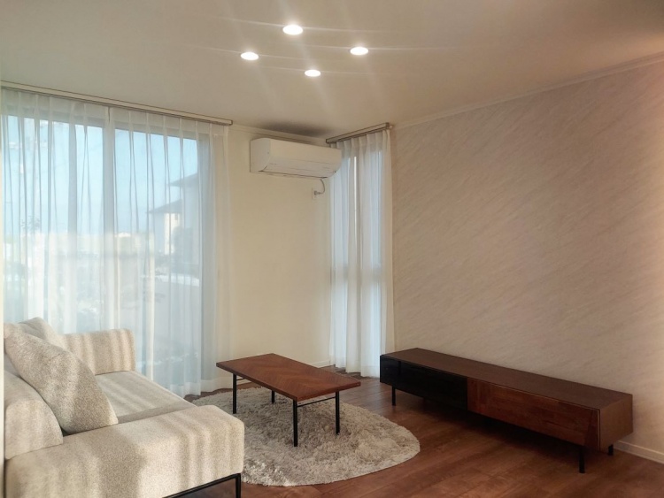 大きな窓から柔らかな光が入り、白いソファと丸いラグが置かれた穏やかなリビングです。