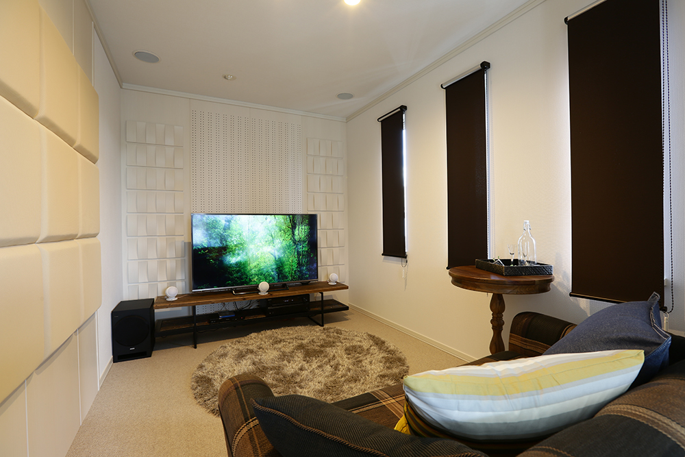 壁に音響パネルが取り付けられたホームシアタールーム。大画面のテレビが中央に配置され、ふわふわのラグが敷かれています。ソファとサイドテーブルが置かれ、リラックスできる空間が広がっています。
