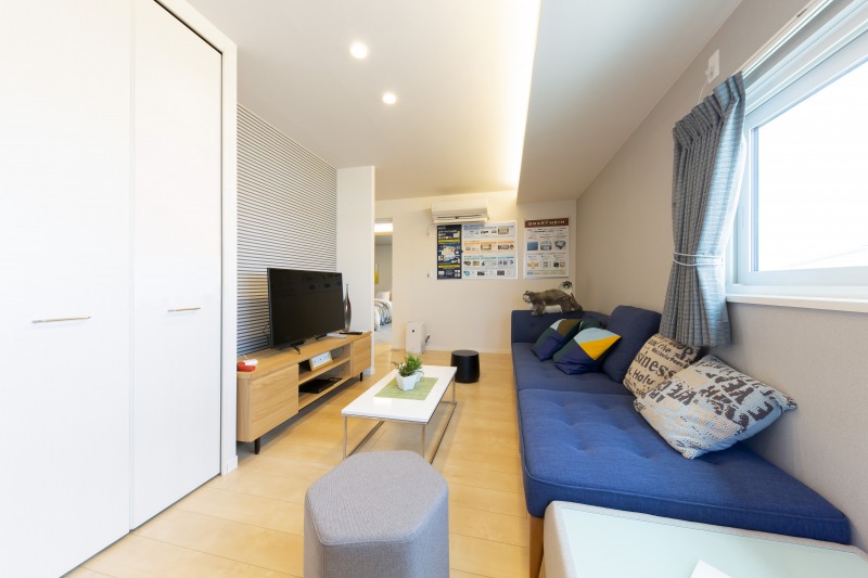 IOT（Internet Of Things）家電を利用したこれからの暮らしを提案した部屋。青いソファとカラフルなクッションが配置され、中央には白いローテーブルがあります。壁にはポスターが貼られ、窓からは明るい光が差し込んでいます。