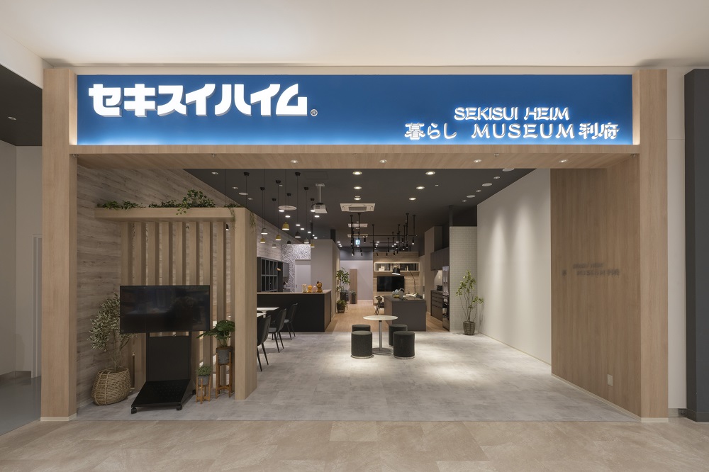 イオンモール新利府南館2階にある、暮らしミュージアム利府のエントランス写真。温かみのある木目調のデザインで、シンプルかつモダンな雰囲気が漂います。入口には座れるスペースがあり、奥にはモデルルームのような展示が広がっています。