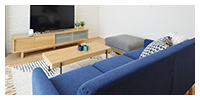 2グリーンな暮らしイメージ画像。青いソファと木製のテーブルが置かれたリビングルーム。奥にはテレビとナチュラルな木目調のテレビ台が見え、シンプルで落ち着いた雰囲気です。