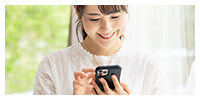 3便利でエコな暮らしイメージ画像。白い服を着た女性がスマートフォンを操作しながら微笑んでいます。背景には緑があり、明るい自然光が差し込んでいます。