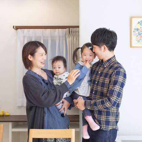 ideal livingイメージ画像。家の中で楽しそうに笑顔を交わす4人家族。母親が赤ちゃんを抱き、父親がもう一人の子供を抱っこしています。温かい雰囲気が伝わります。
