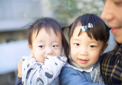 ideal livingイメージ画像。赤ちゃんと幼児が寄り添って笑顔を見せている写真。幼児はリボンをつけて優しい表情をしており、赤ちゃんは手を口に当てています。
