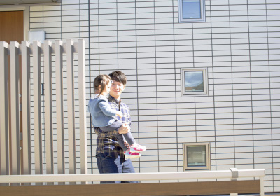 現在のお住いの お気に入りのスペースイメージ画像。父親が子供を抱きかかえて家の前を歩いています。明るい日差しが差し込む中、穏やかなひとときを過ごしています。