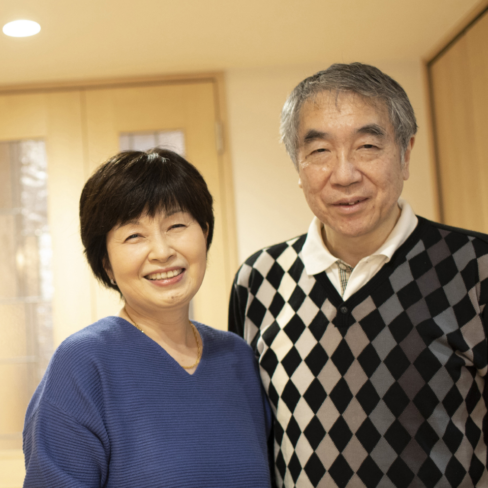 室内で微笑むシニア夫婦が並んで立っている写真です。