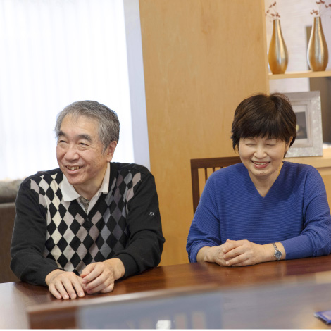 eventuallyイメージ画像。年配の男女がテーブルに向かって座り、笑顔で会話を楽しんでいます。暖かい雰囲気の部屋で、背後には飾り棚があります。