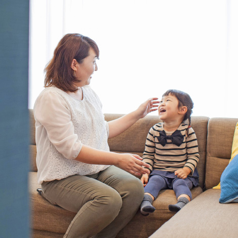 Good timingのイメージ画像。母親と幼い女の子がソファに座り、笑顔で向き合っています。母親は娘の頭に手をやりながら、女の子の笑顔を楽しんでいる様子です。明るい部屋の中で、穏やかな親子の時間が流れています。