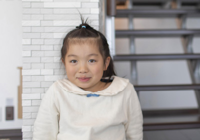 Second livingイメージ画像。階段の前でポーズを取る女の子。白いトップスを着て、髪を結んだ女の子が少し恥ずかしそうに笑っています。背後には階段が見え、明るい空間に佇む可愛らしい姿が印象的です。