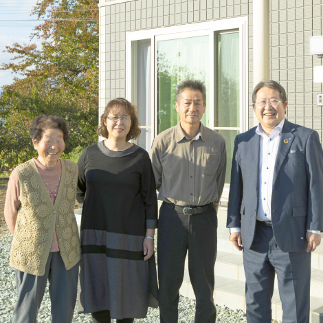 Encounterイメージ画像。家の前で笑顔の家族とスーツ姿の担当営業の男性が並んで立っています。明るい日差しの中、家族は仲良く並んで、和やかな雰囲気が感じられ、背後には家の外観と庭が見えます。