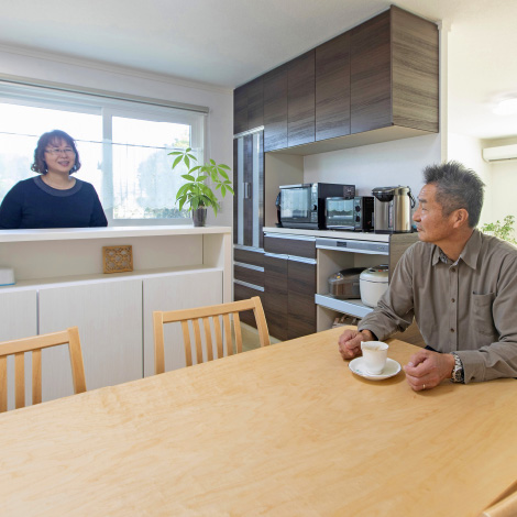 Flow lineイメージ画像。キッチンカウンター越しに笑顔で会話する夫婦。妻は窓際に立ち、夫はダイニングテーブルでコーヒーカップを手に持っています。キッチンには家電が整然と並び、明るい光が差し込む温かい雰囲気の空間です。