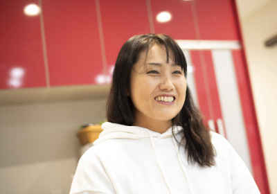 Worm houseイメージ画像。白いパーカーを着た女性が、笑顔で楽しそうにしています。背後には赤いキッチンのキャビネットが見え、明るい室内の雰囲気が伝わります。
