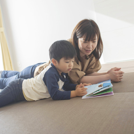 Relax timesのイメージ画像。母親と息子が床に寝転びながら一緒に絵本を読んでいます。二人は真剣な表情でページを見つめており、親子の温かい交流が感じられる静かなひととき。柔らかな光が部屋に差し込んでいます。