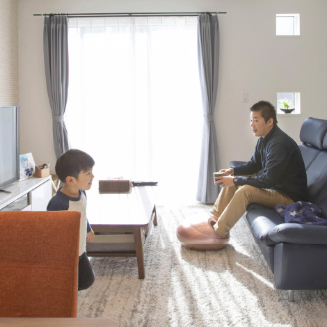 Will welcomeのイメージ写真。リビングで父親がソファに座り、息子と向き合っています。父親はリラックスしてカップを持ち、息子は少し前に立っていて、大きな窓から明るい光が差し込み、穏やかな時間が流れる部屋の一場面です。