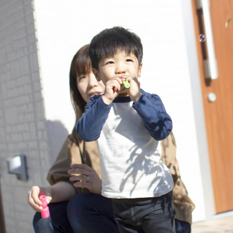 Open spaceイメージ写真。幼い男の子がシャボン玉を吹いて楽しんでいます。後ろには母親が微笑みながら見守っていて、晴れた日の明るい光の中で、親子が楽しい時間を過ごしている様子が伝わります。