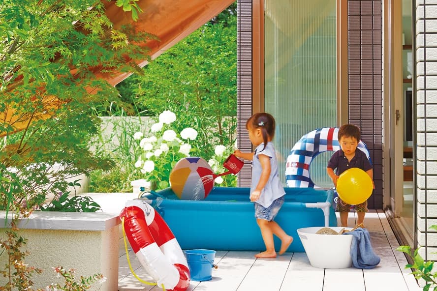 外とつながるのイメージ画像。“庭に設置されたビニールプールで、子どもたちが水遊びをして楽しんでいます。プールの周りには浮き輪やビーチボールがあり、緑豊かな庭に囲まれたリラックスできる環境です。