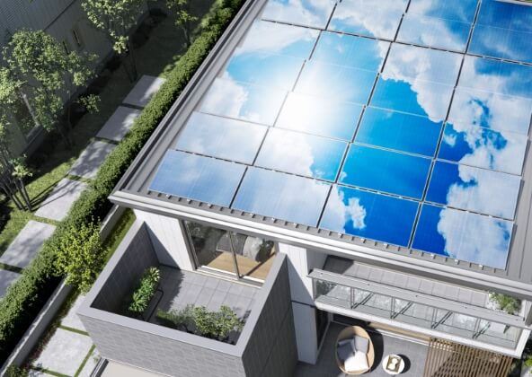 クリーンエネルギー活用のイメージ画像。屋根に取り付けられた大きな太陽光パネルが、青空と雲を反射して輝いている様子。環境に優しいエネルギーを利用する住宅の一部を示しています。