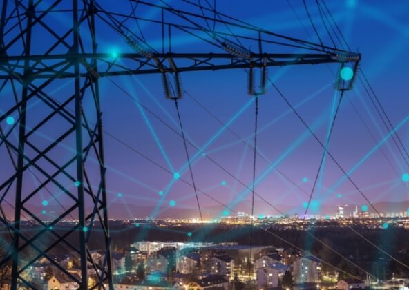 エネルギーシェアのイメージ画像。夜の街を背景に、高電圧送電塔と電線が広がり、青い光で結ばれたエネルギーネットワークのイメージが重ねられている。