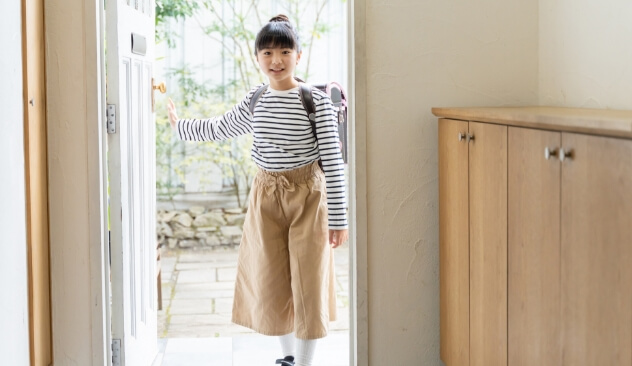 スマホに通知のイメージ画像。ランドセルを背負った女の子が笑顔で玄関のドアを開けて家に帰ってきた様子です。明るい玄関と外の庭が見えています。
