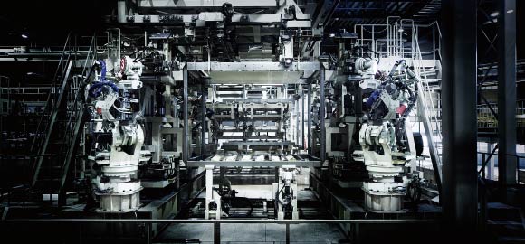 雨風の影響を抑えるのイメージ画像。大型の産業用ロボットアームが並んだ自動化された工場の内部。機械が金属フレームや部品を正確に操作し、製造プロセスを進めています。